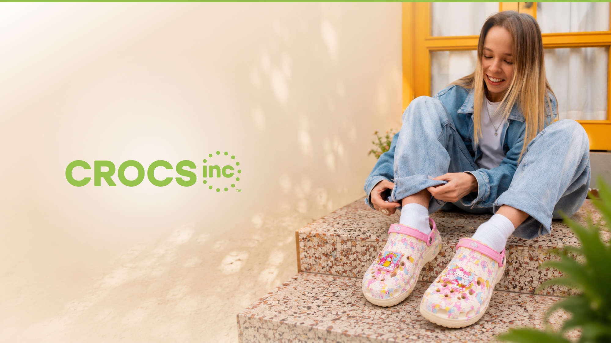 S11-Last Slide-after After Redesigned end slide using a full-bleed lifestyle photograph of a young woman in a denim outfit sitting on stone steps and adjusting a pair of white Crocs clogs decorated with floral Jibbitz charms, with the Crocs Inc logo in green type placed on the left half of the slide over a warm cream-toned wall background.