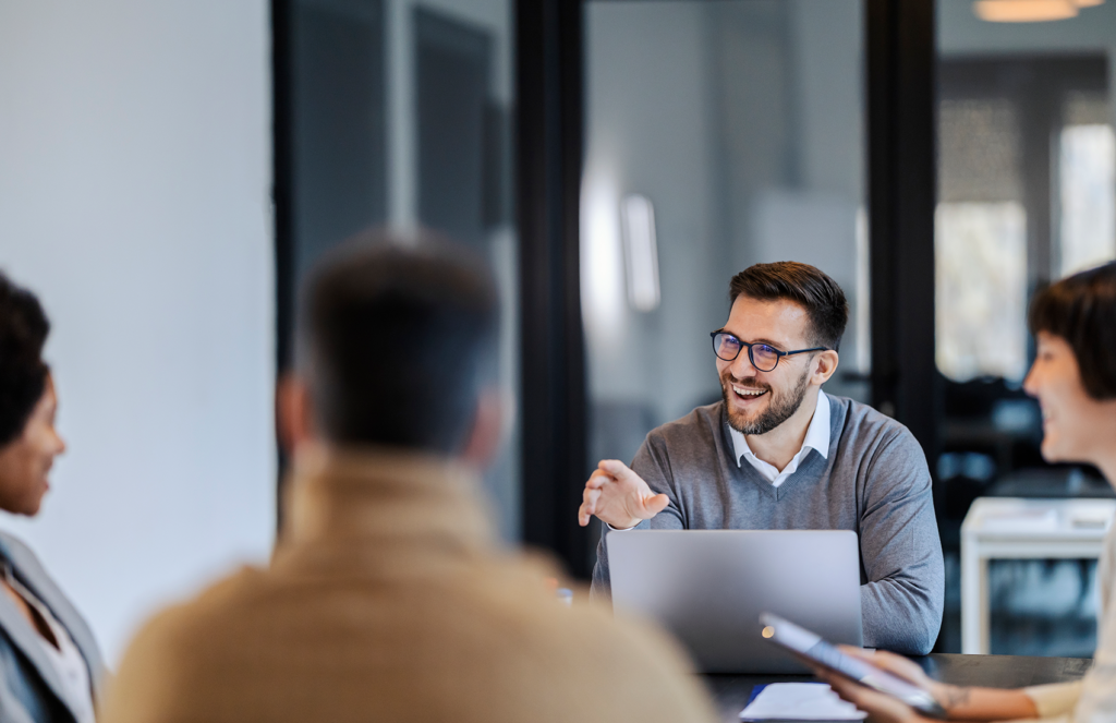 Smiling professional presenting to colleagues in a meeting – showcasing three key principles behind making impressive consulting-style presentations for impactful communication and client engagement.